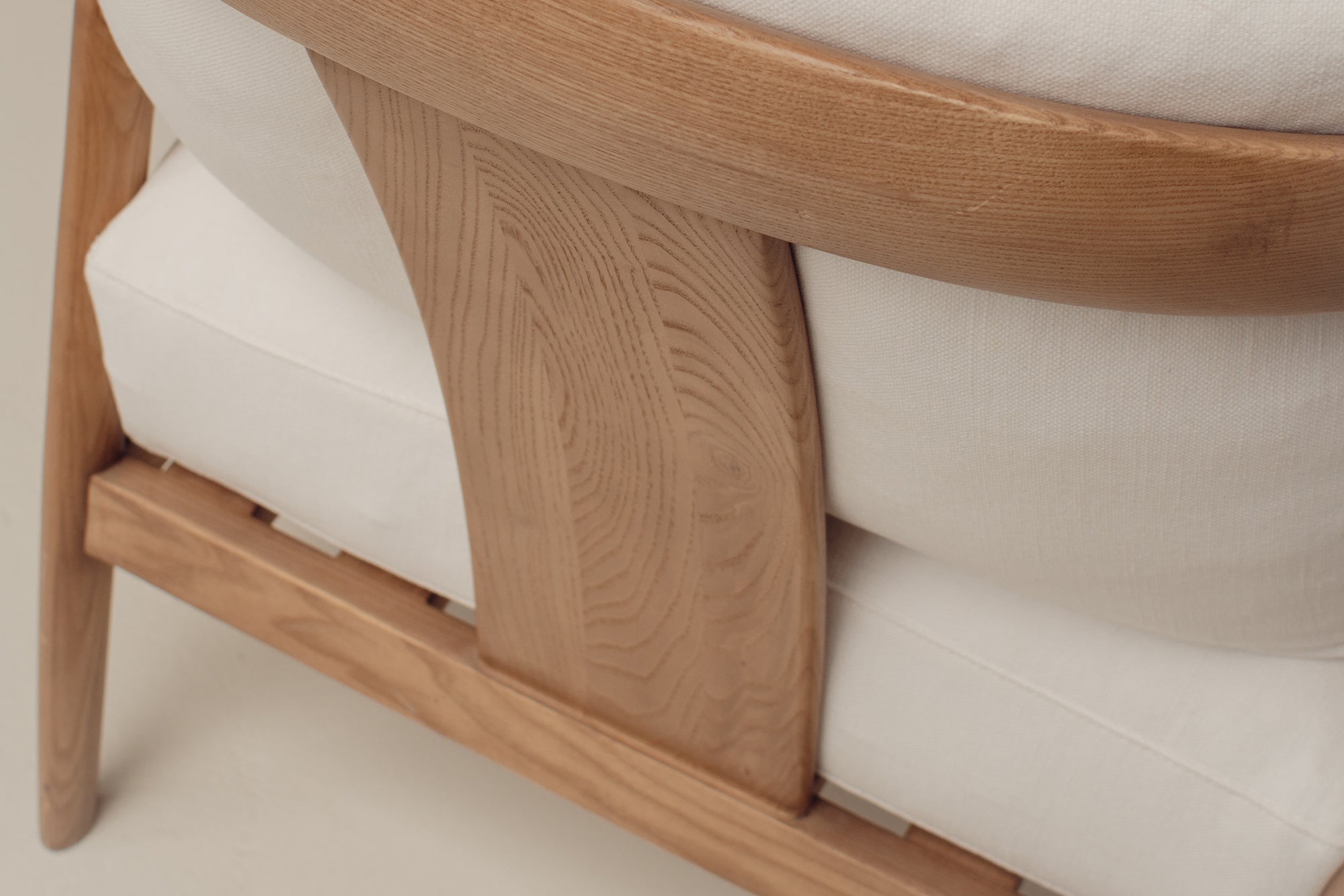 Close-up of a wooden armchair with a light oak frame and off-white cushions, showing the grain and texture of the wood and fabric.