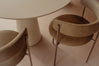 A close-up view of two modern upholstered dining chairs with a warm taupe-brown vinyl finish and slim metal legs, positioned around a round table on a matching beige floor.