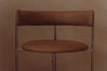 A close-up of a modern dining chair with a curved back and seat in warm brown leather, supported by slim dark metal legs.
