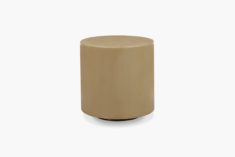 A minimalist cylindrical side table or stool in a warm taupe-beige finish, shown from a three-quarter angle on a clean white background.