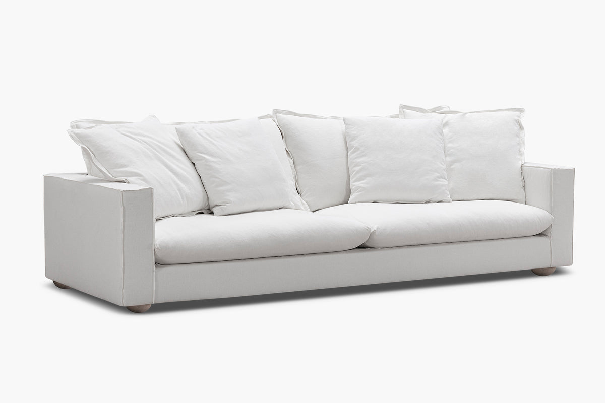 White sofa with plush cushions and rounded wooden feet photographed at an angle.