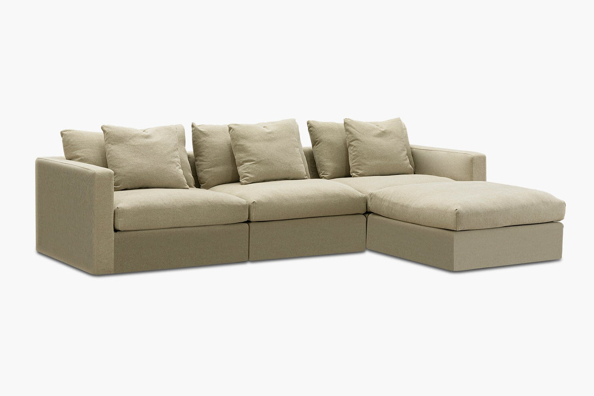 Beige linen sofa with ottoman chaise and three back cushions, studio angled view