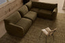 Olive green modular corner sofa viewed from above in a room with a distressed wall.