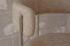 Close-up of a modern upholstered chair with a rounded beige leather backrest and a slim metallic silver frame, set against a textured gray plaster wall.