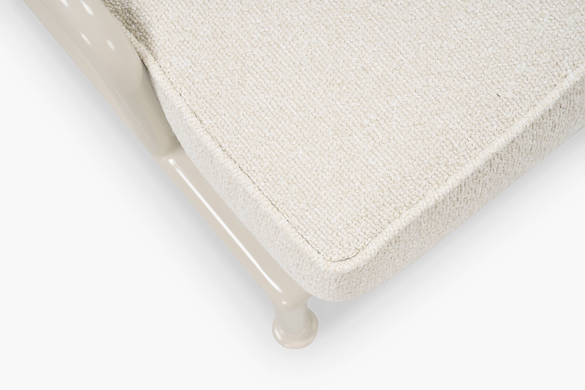 Close-up corner of cream boucle cushion and glossy tan frame leg on a lounge chair