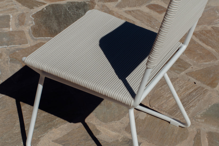Close-up of a white rope dining chair seat on a stone patio
