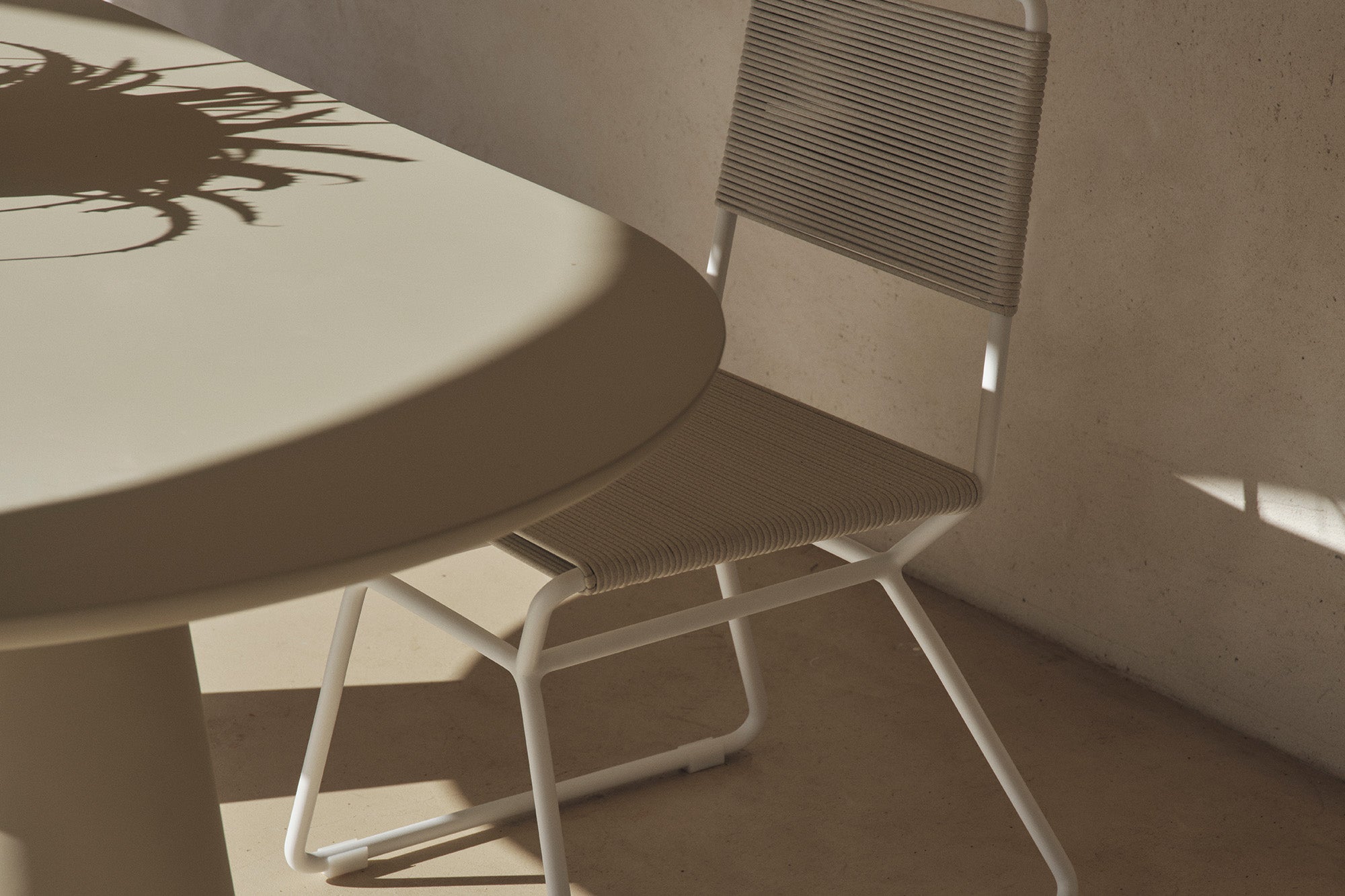 Rope dining chair at a table beside a sunlit stone wall