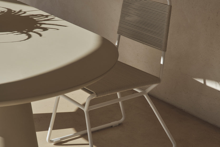 Rope dining chair at a table beside a sunlit stone wall