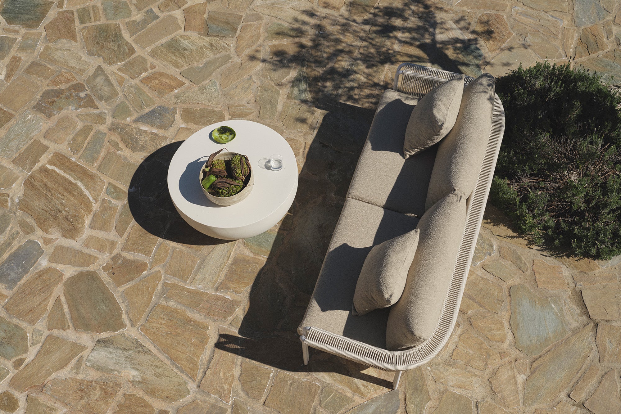 Overhead view of beige sofa and round table on stone patio