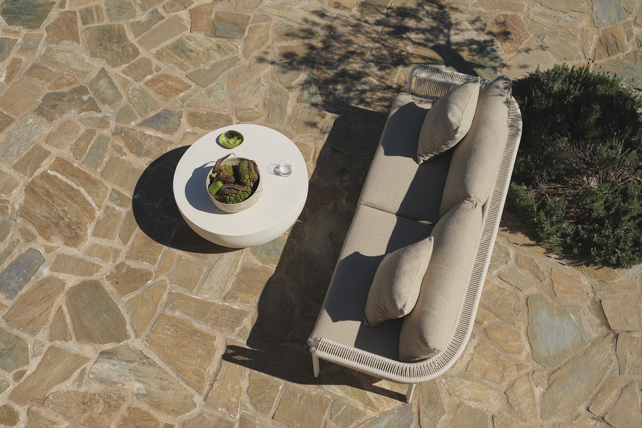 Overhead view of beige sofa and round table on stone patio
