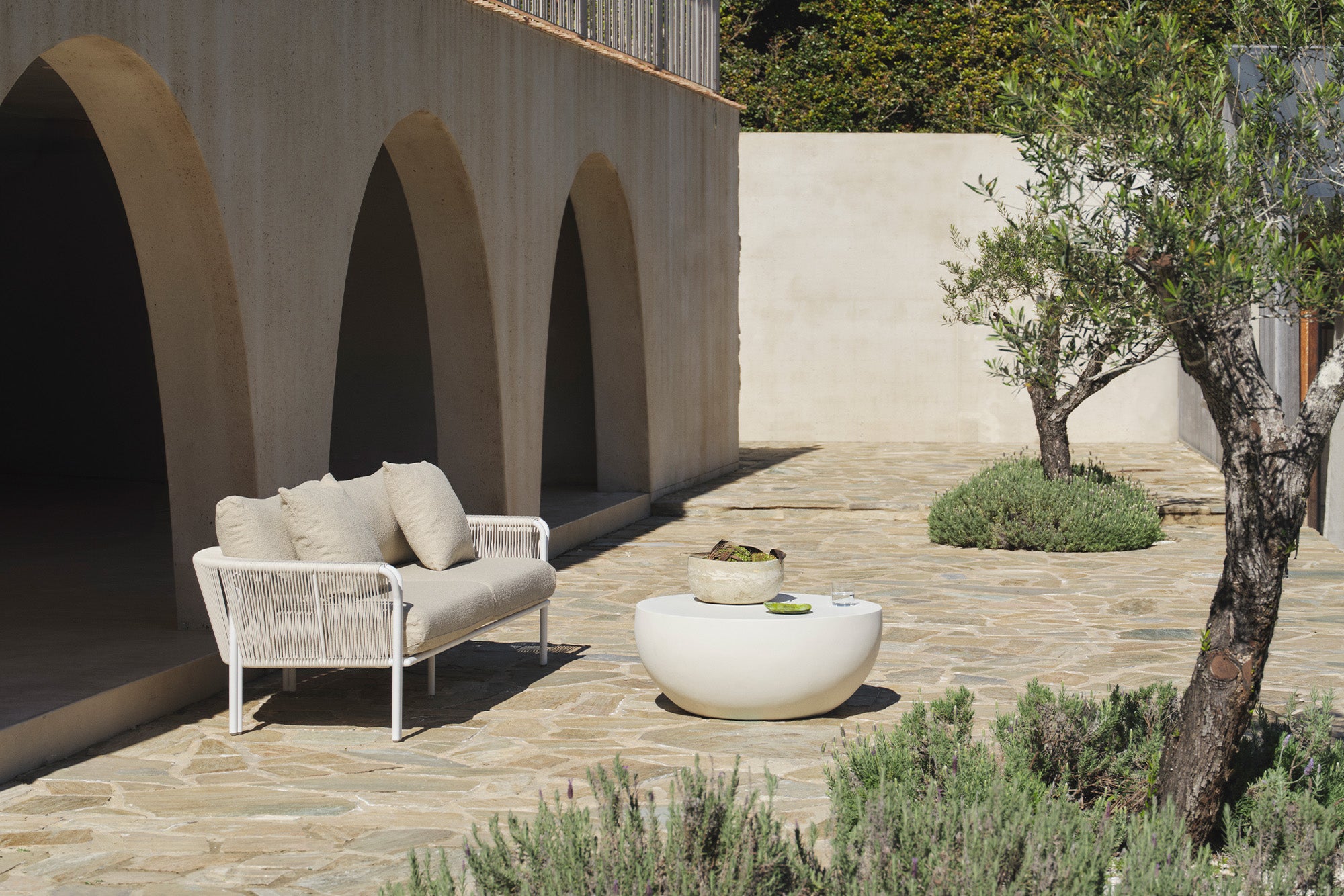 Beige boucle sofa under a stone archway beside an olive tree