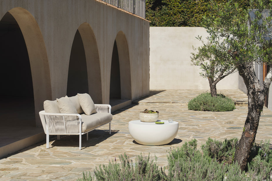 Beige boucle sofa under a stone archway beside an olive tree