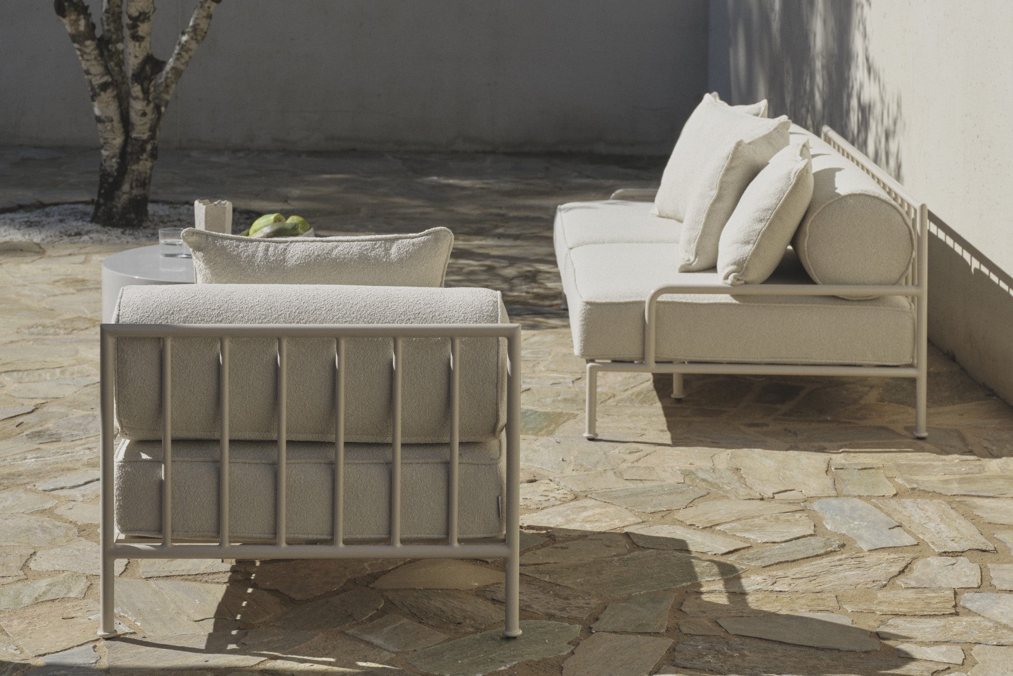 Lounge chair and sofa on stone patio beside a tree and table