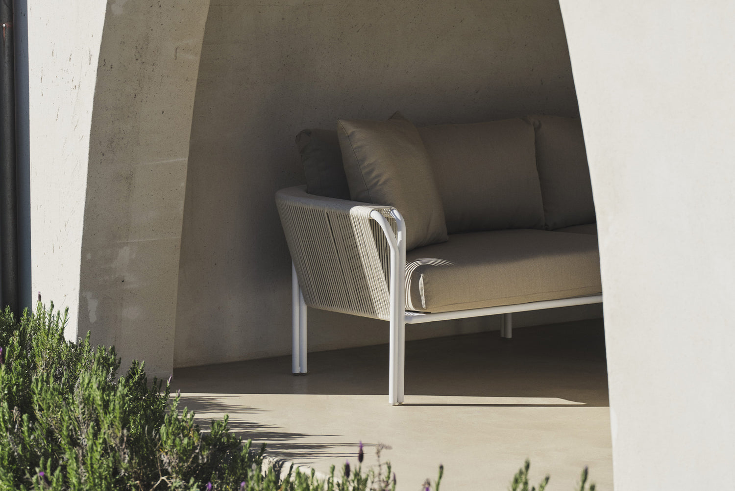 Beige linen sofa under a stone archway beside lavender bushes