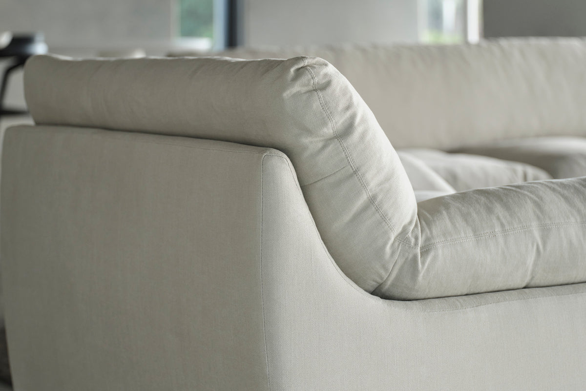Close-up of a cream sofa arm and back cushion beside a window.