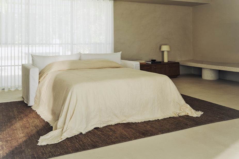 Cream sofa bed with a linen throw draped over the mattress in a sunlit bedroom.