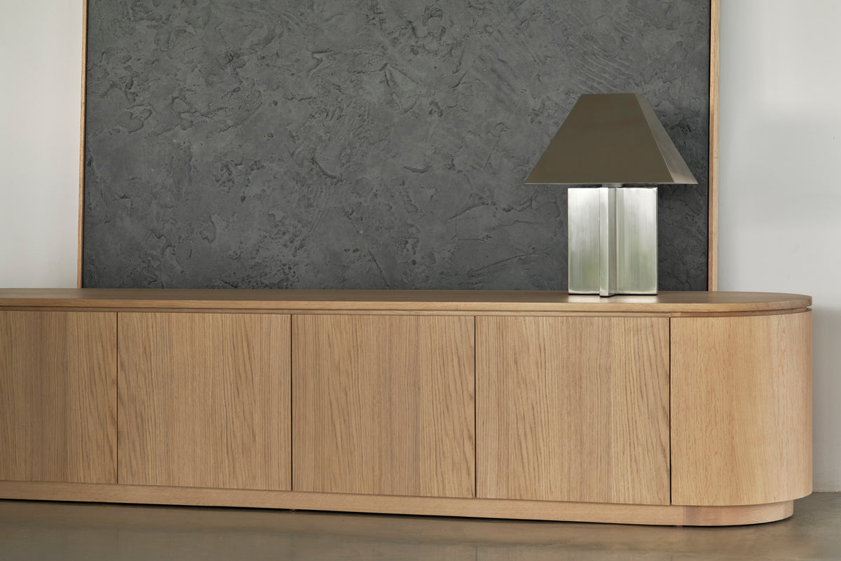 Wooden sideboard with a lamp against a textured wall.