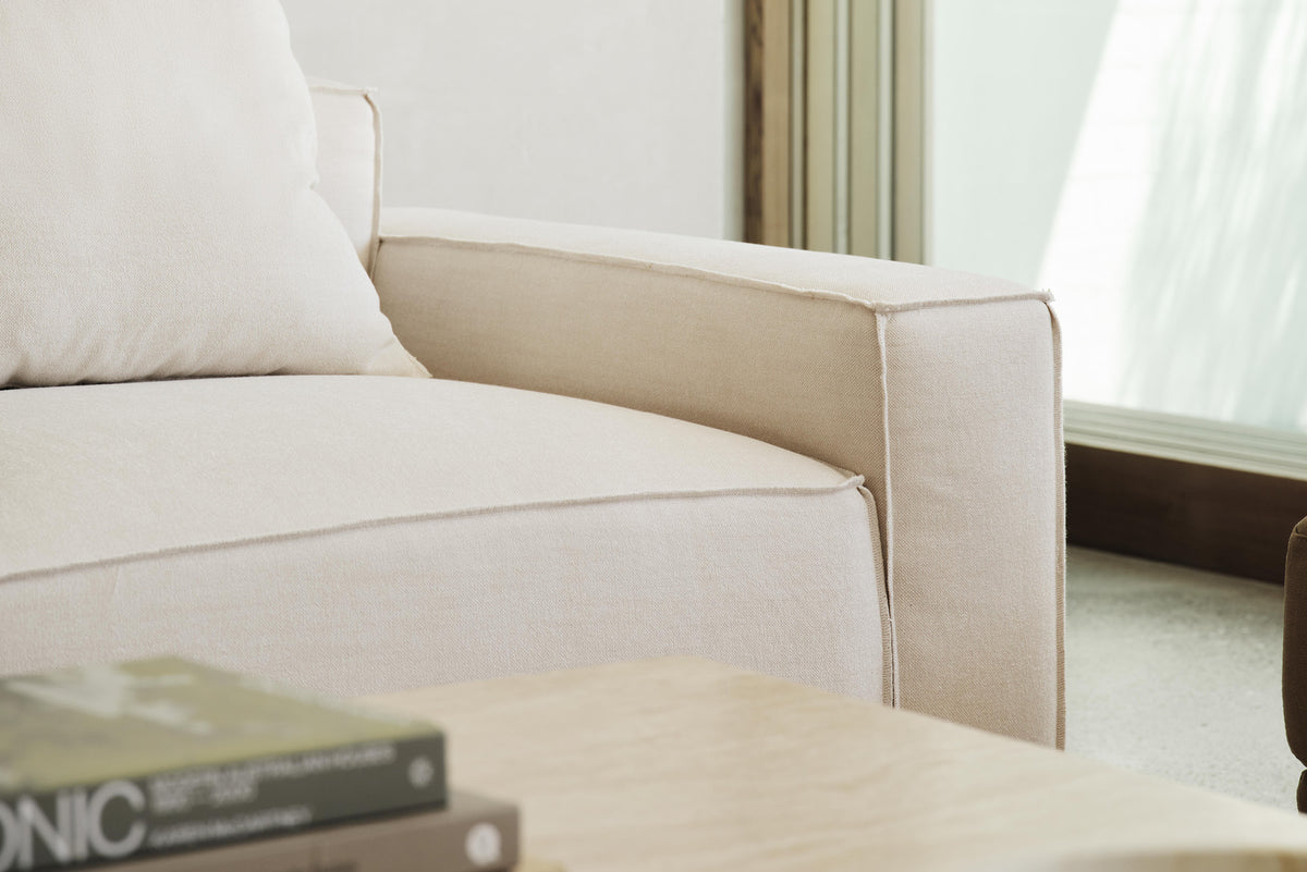 Close-up of a cream sofa arm beside a coffee table stacked with books.