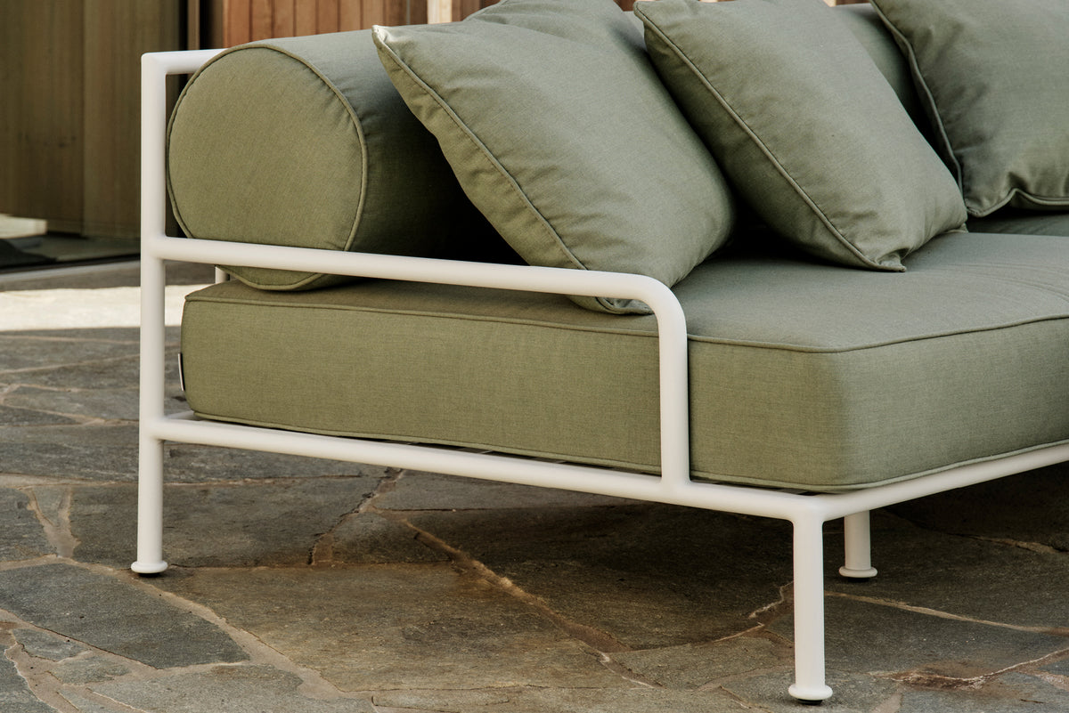 Sage green outdoor sofa arm and bolster cushions on a stone patio