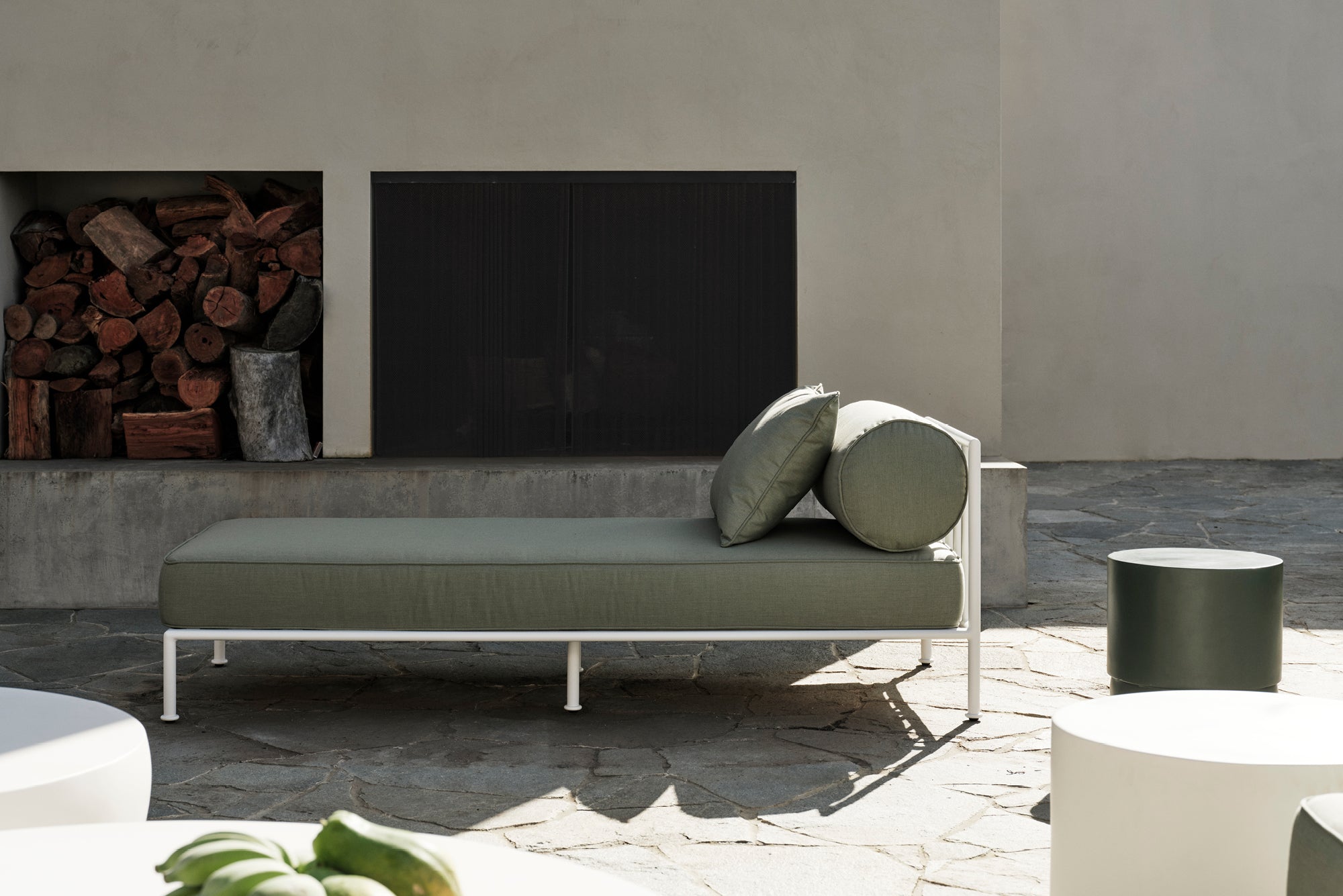 Modern outdoor sofa with cushions in a patio setting with firewood and a television.