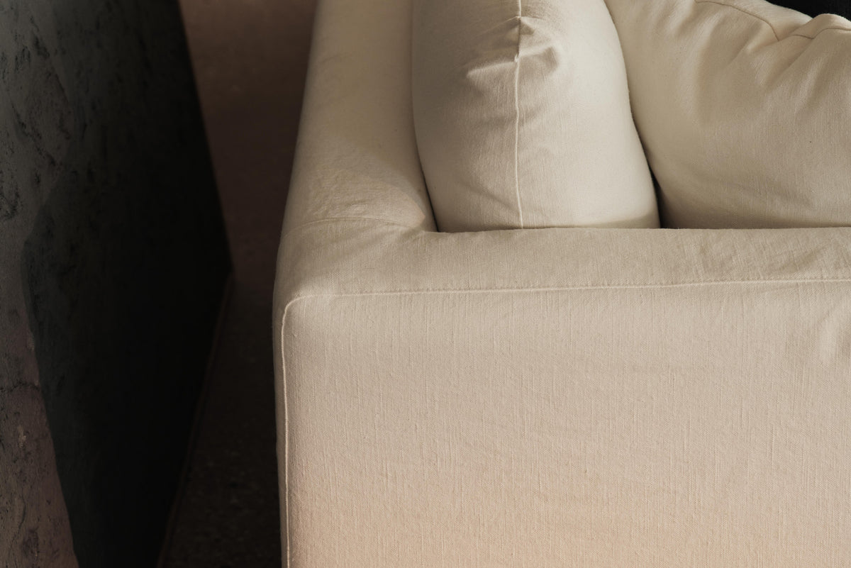 Close-up of cream sofa corner and back cushion beside dark textured wall