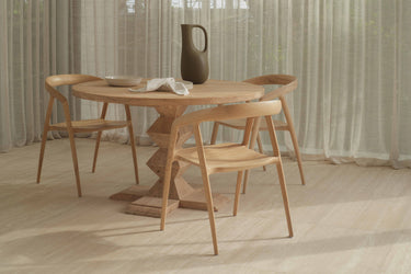 A modern dining chair made of ash timber, with a natural colour, arranged around a dining table in a minimalist style interior.
