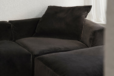 Close-up of black velvet corner sofa beside a sheer curtain