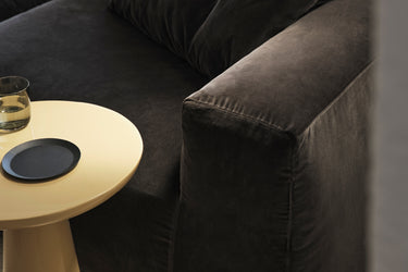 Close-up of dark velvet sofa arm beside a round cream side table