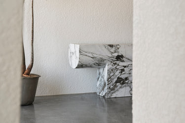 Marble-patterned console against a plain wall with a plant on a concrete floor.