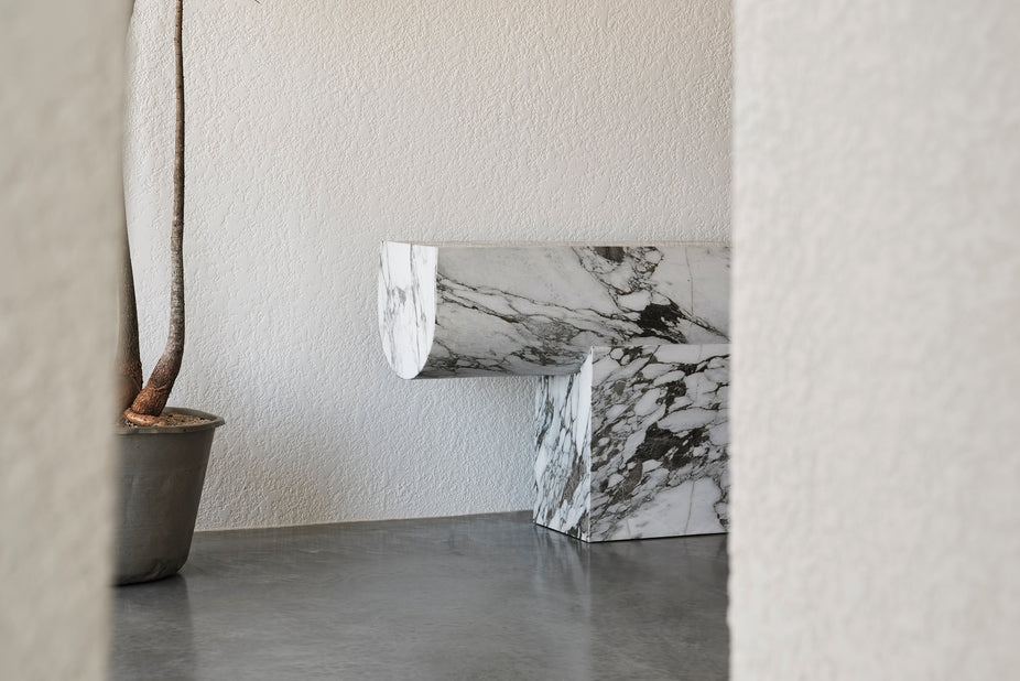 Marble-patterned console against a plain wall with a plant on a concrete floor.