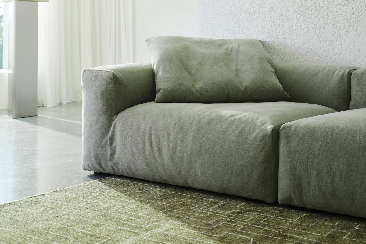 Sage green sofa in a bright room with sheer curtains and a patterned rug