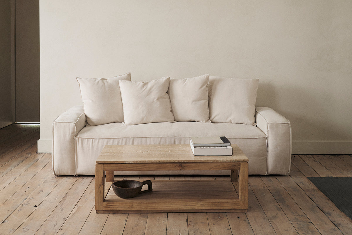 Cream sofa in sunlit living room with round wood coffee table and book