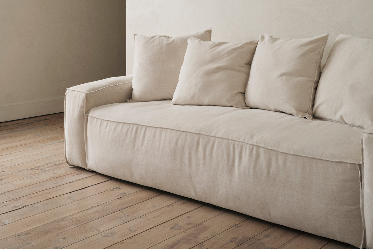 Close-up of a cream sofa arm resting on a wide-plank wood floor.